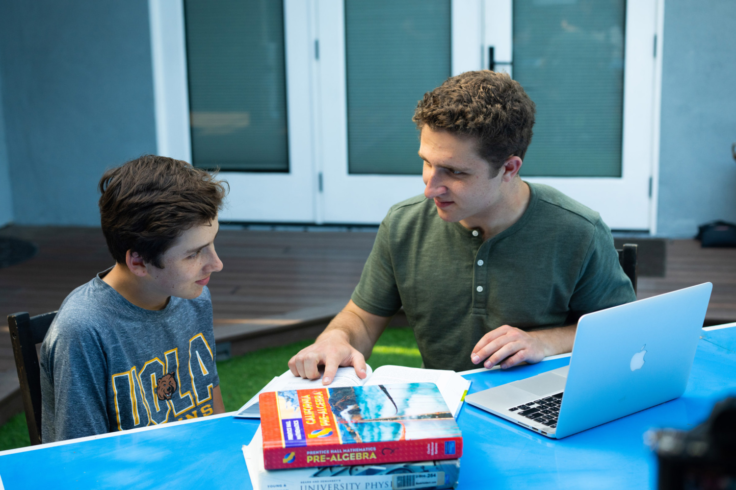Jonah sits with a younger student at a table with a laptop and textbooks.
