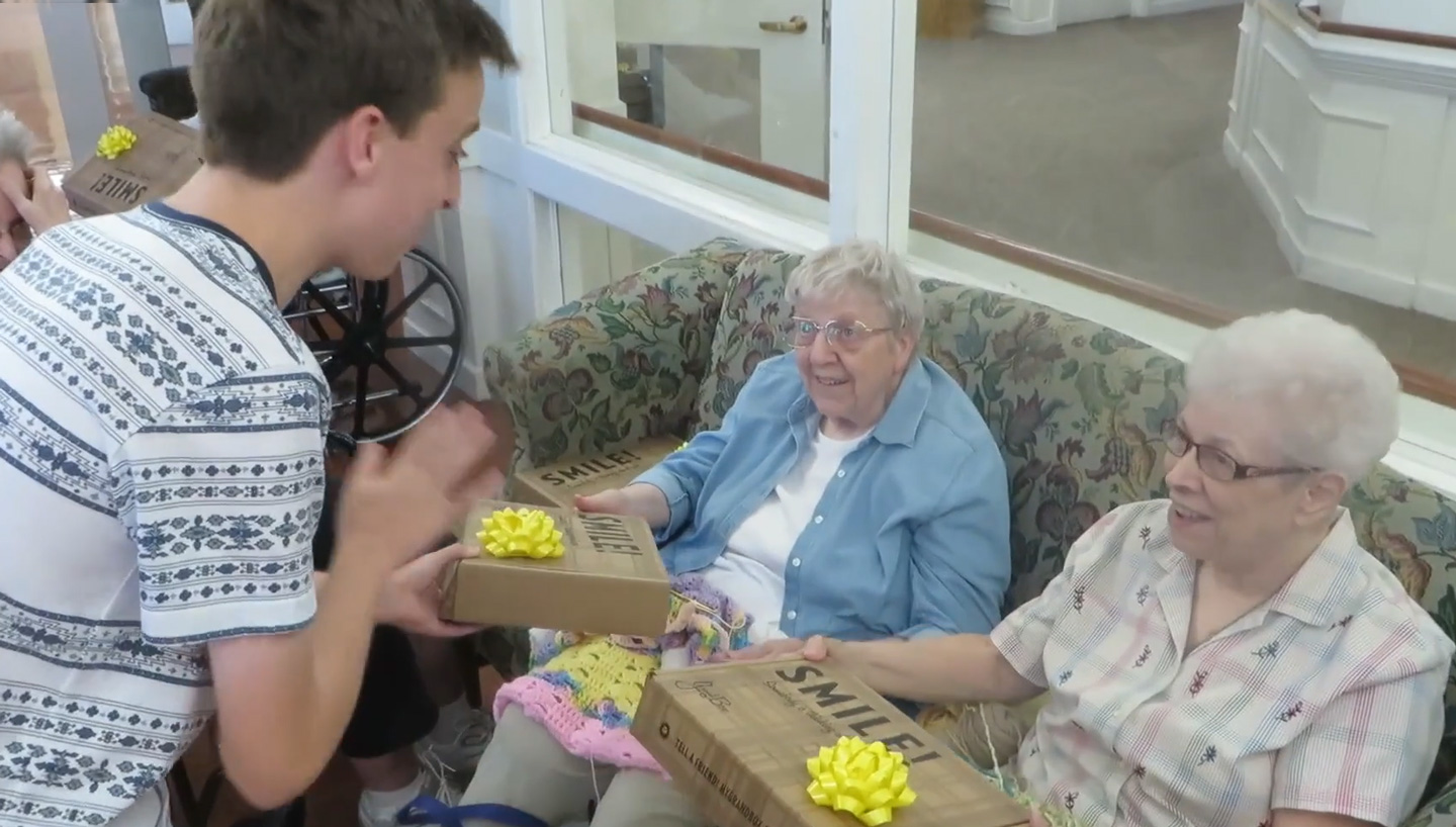 Jacob hands gift boxes to two elderly women.