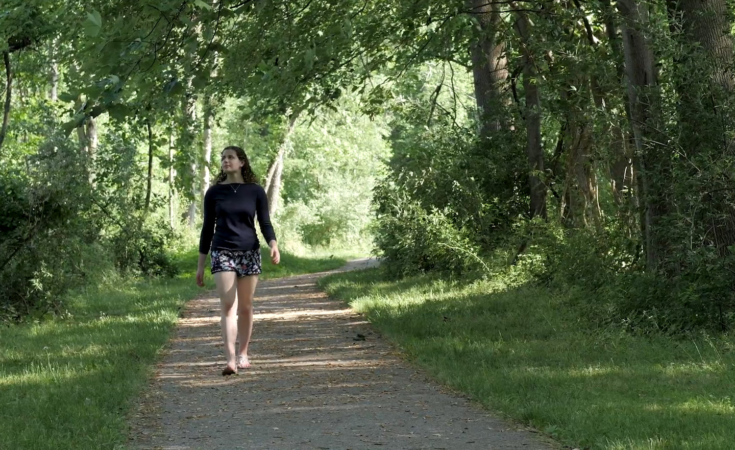 Liza walking down a path in a wooded area.