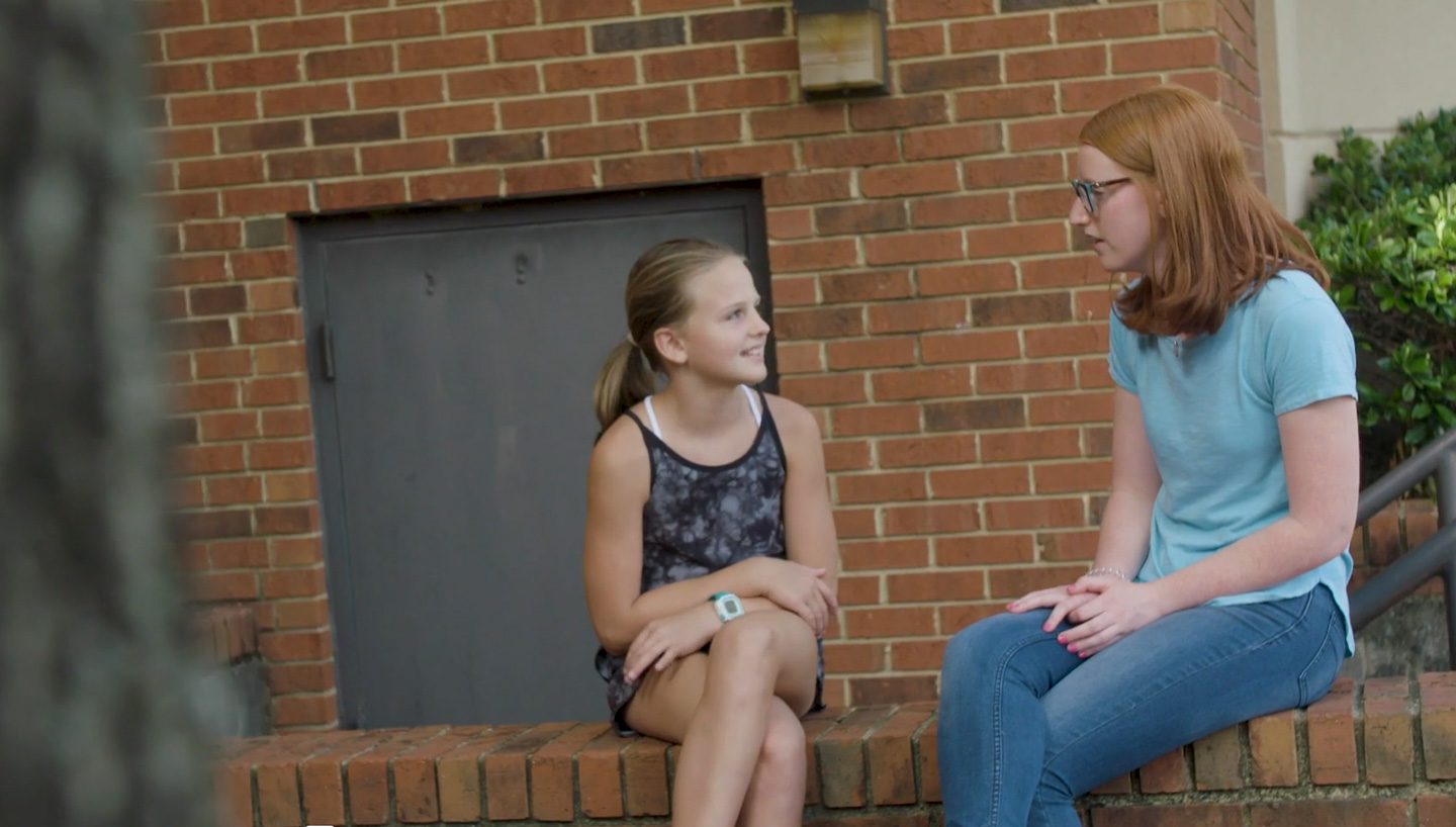 Katelyn McInerney sits with a young girl on a brick wall.