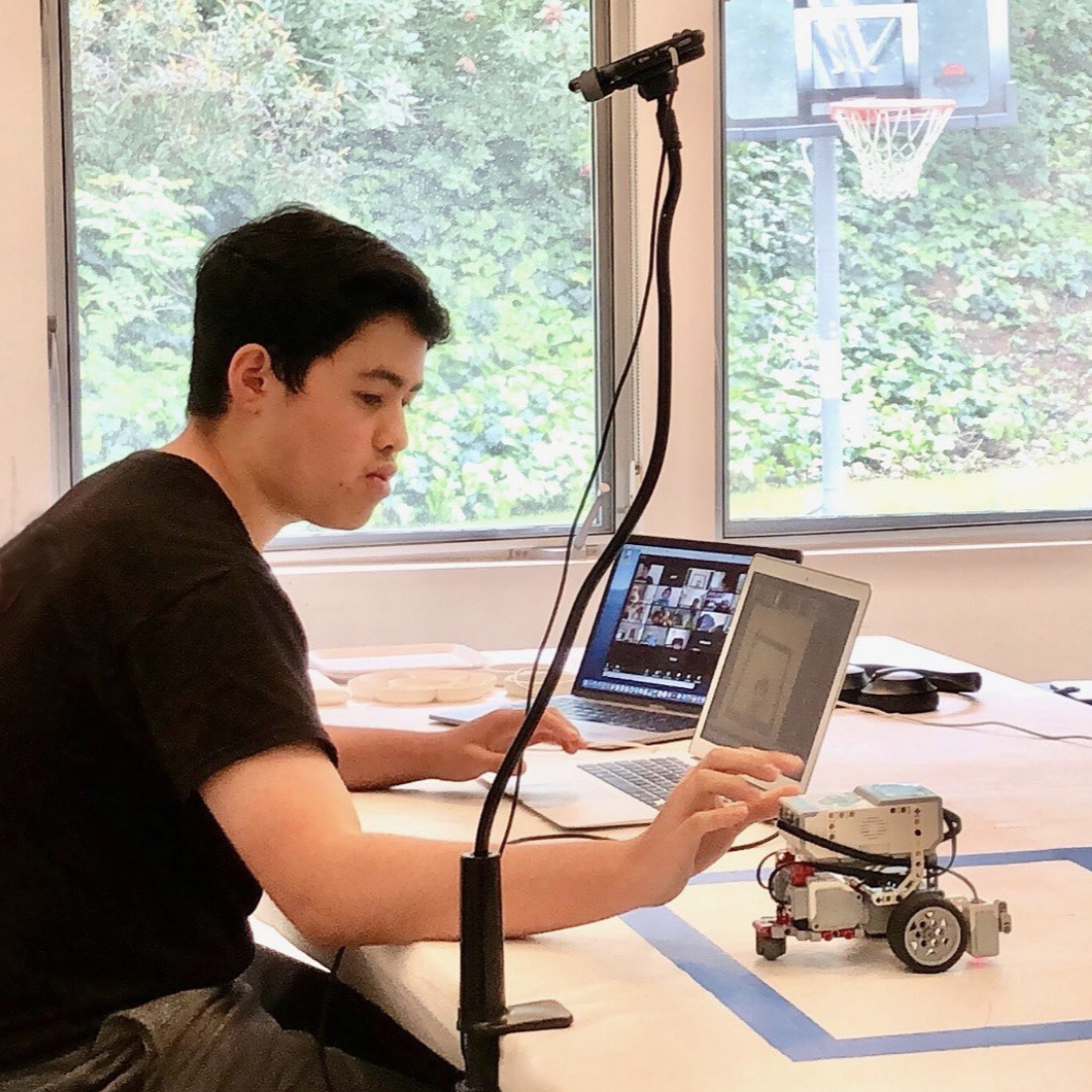 A student working at a desk with a laptop and a small robot.