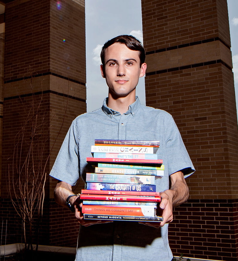 A teen boy stands outside holding a stack of banned books.