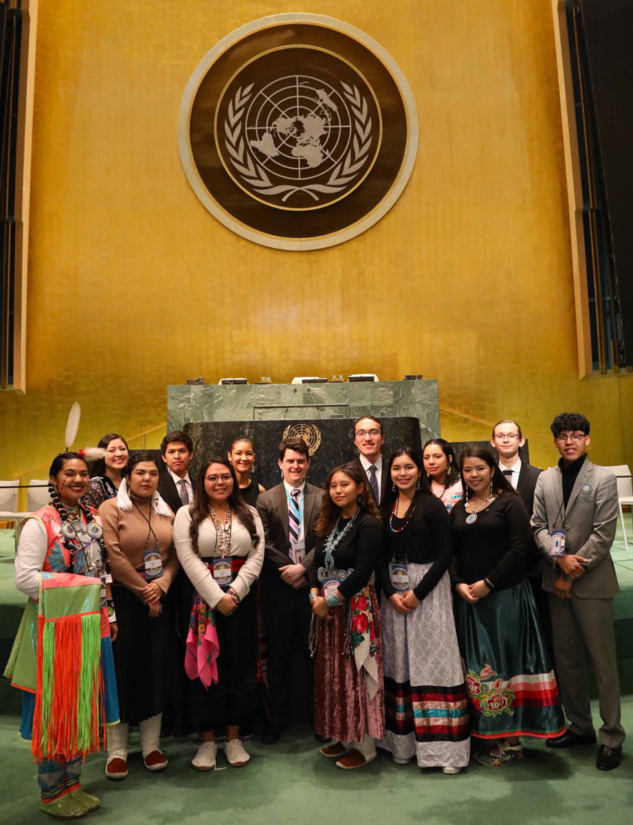 Nathan and a group of young adults, some in indigenous dress, standing in front of the United Nations podium.