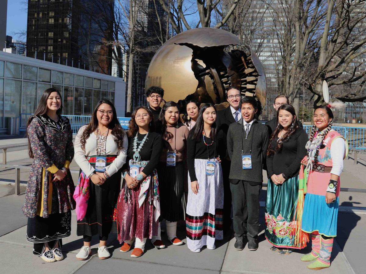 Nathan and a group of teens, most in Native American dress, standing outside the United Nations building.