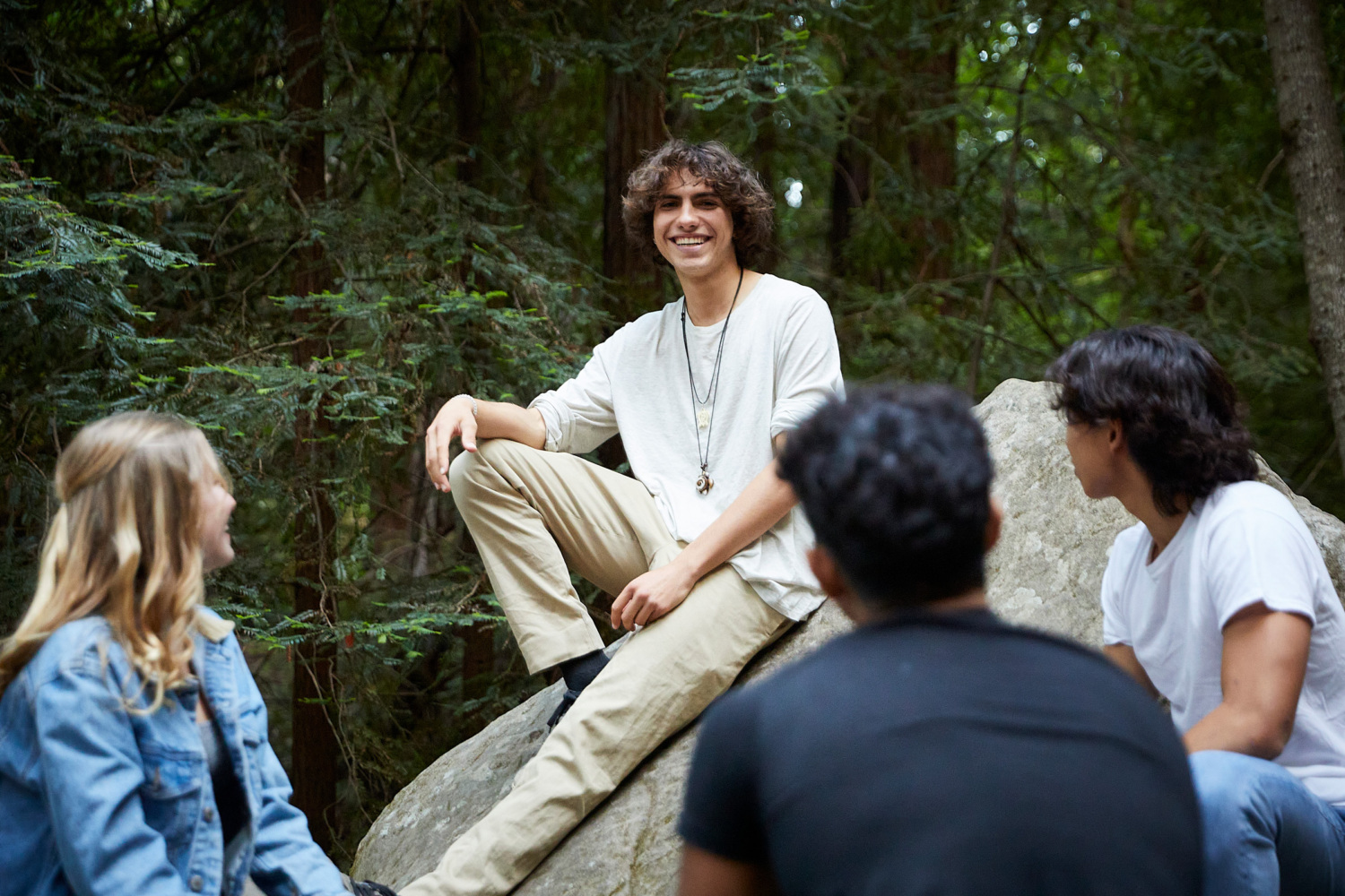 Julian Berkowitz-Sklar sits on a large rock smiling with other students sitting around him.
