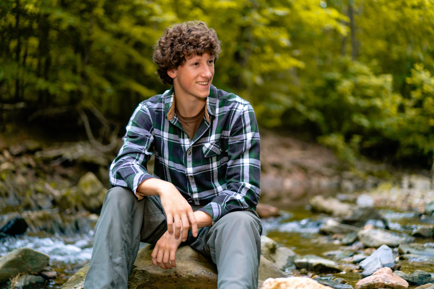 Max Blacksten sitting on a large rock along a river
