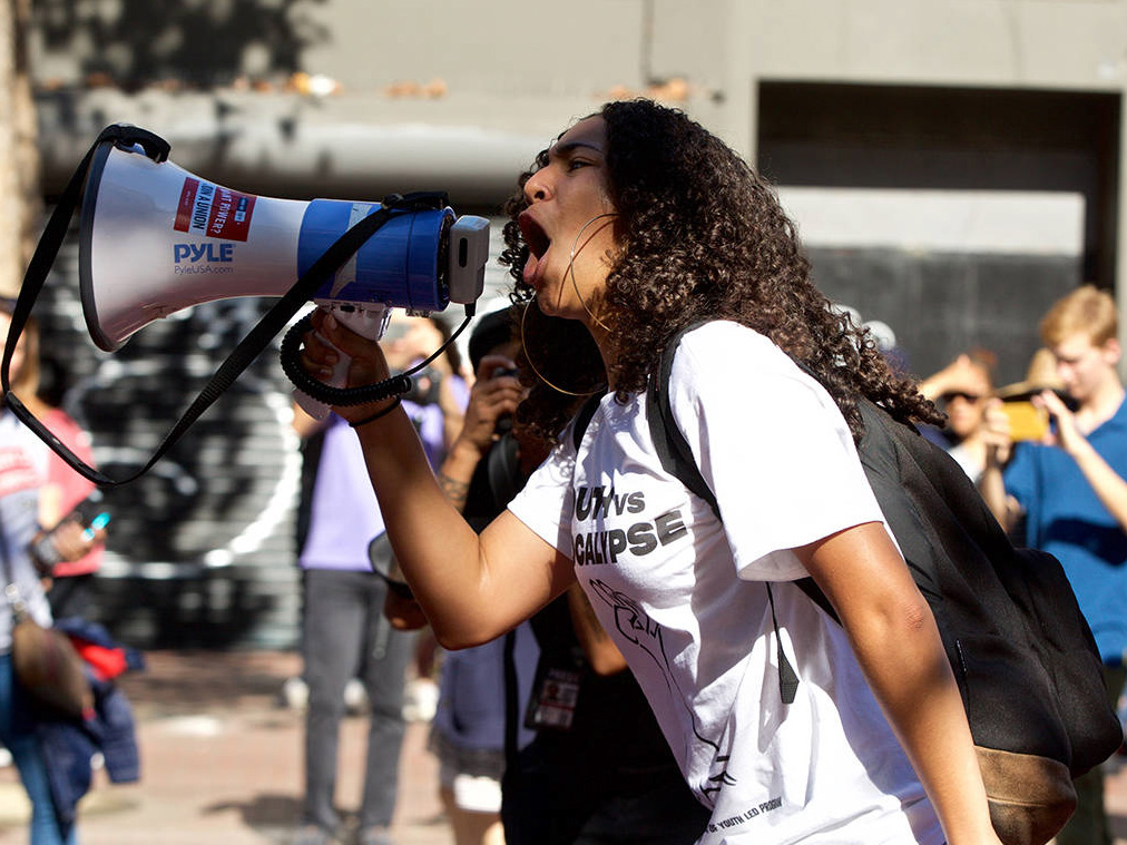Isha is outside at a rally holding a megaphone and shouting into it.