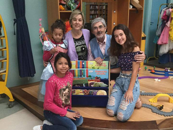 Beatriz kneeling with two educators and two students by a display case of children's books.