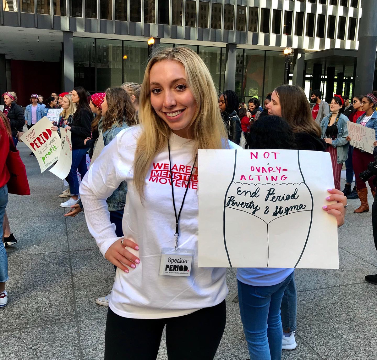 Sophie standing outside at a rally holding a sign that says "Not ovary acting end period poverty and stigma".