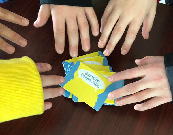 Several hands reach for a stack of "Question Connection" cards that are on a table.