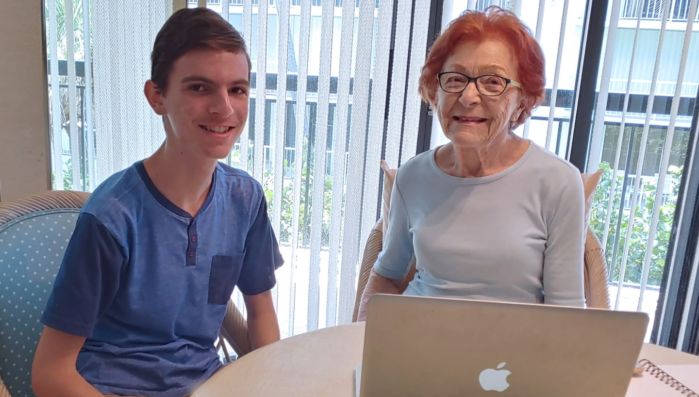 Sam sits with an elderly woman in front of her laptop,