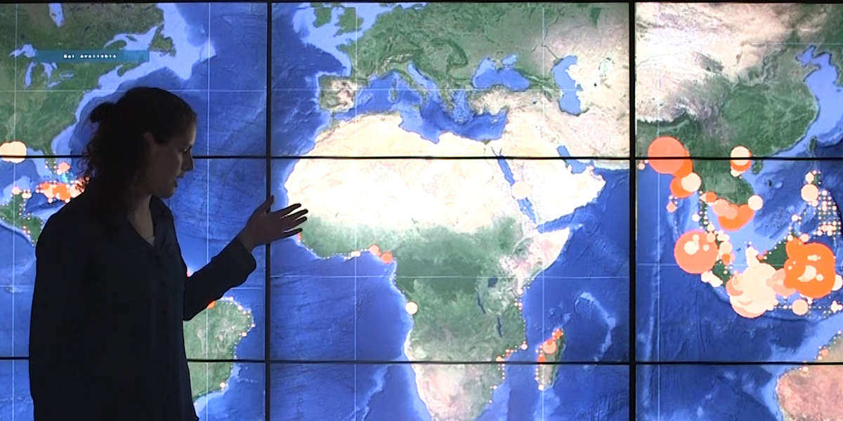 Liza standing in front of an illuminated world map pointing to the country of Africa.