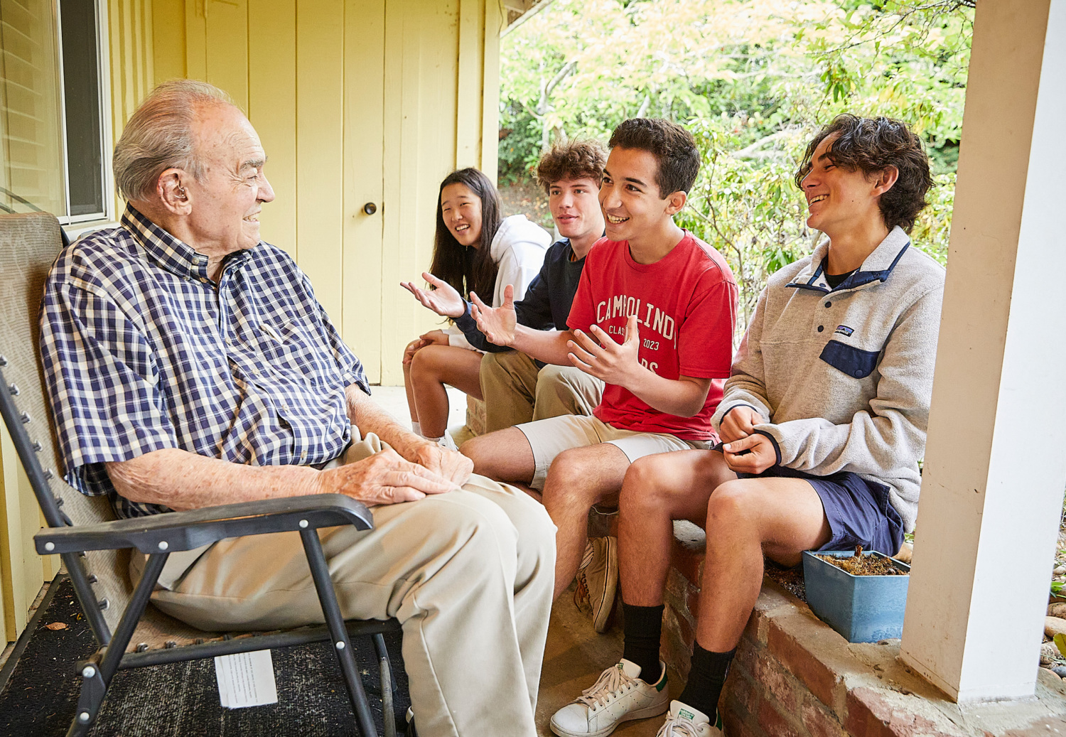 Jake Hammerman and 3 other teens visit on a porch with an elderly man.