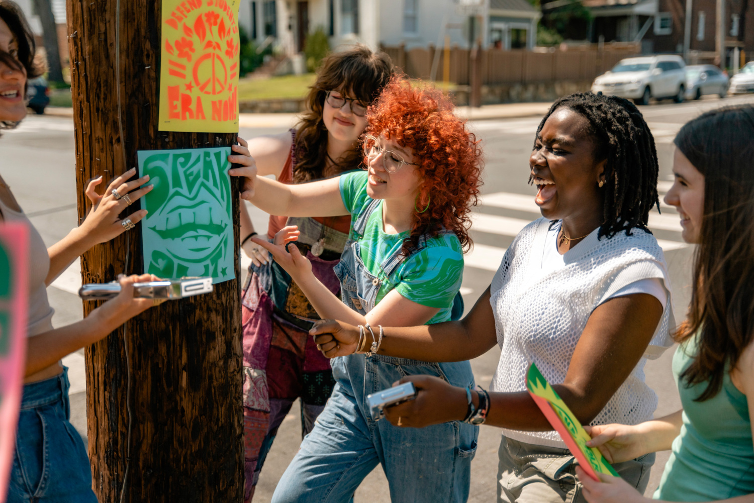 Anabelle Lombard and several other teen girls staple a sign to a utility pole.