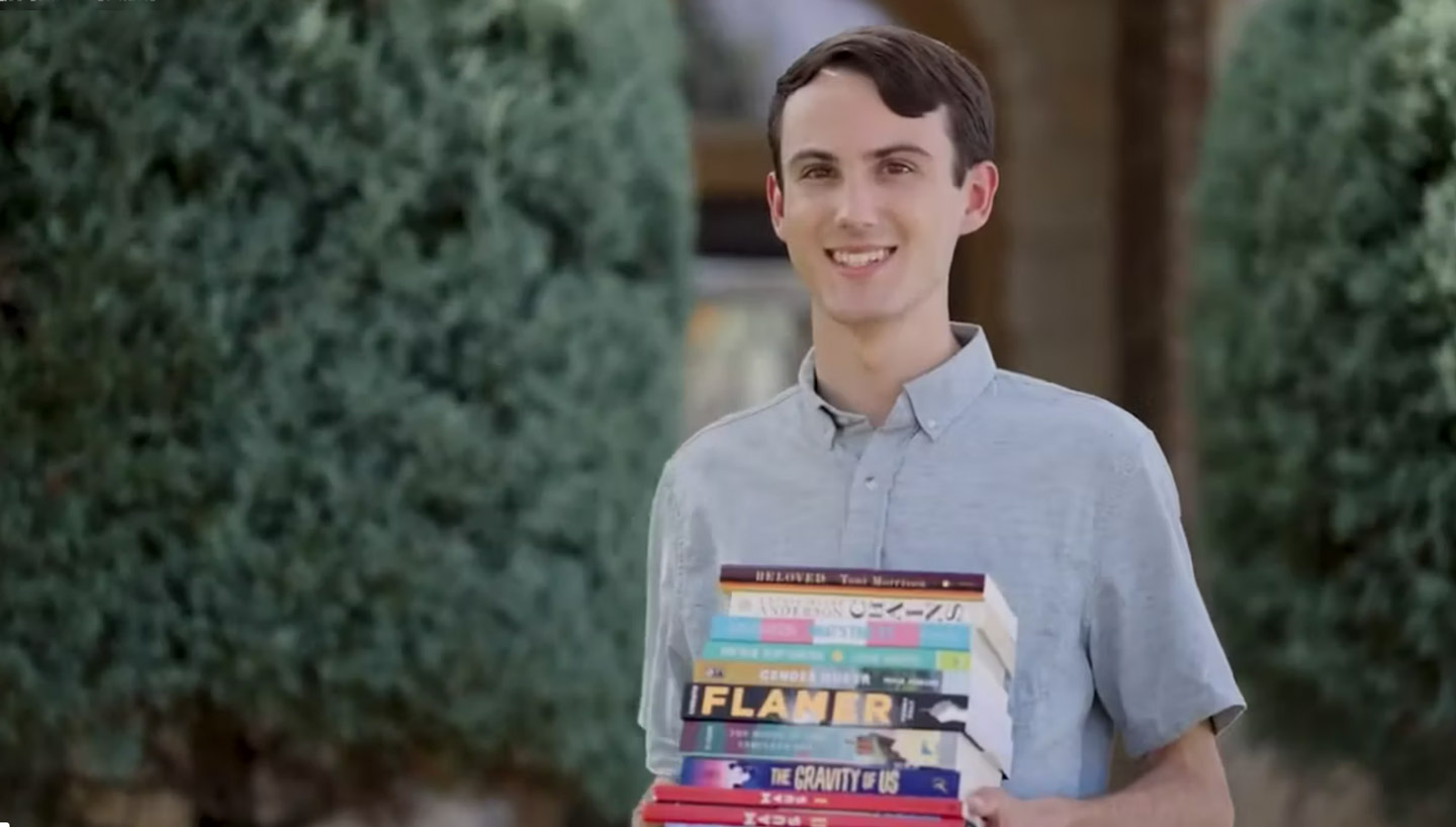Cameron standing outside holding a stack of banned books.