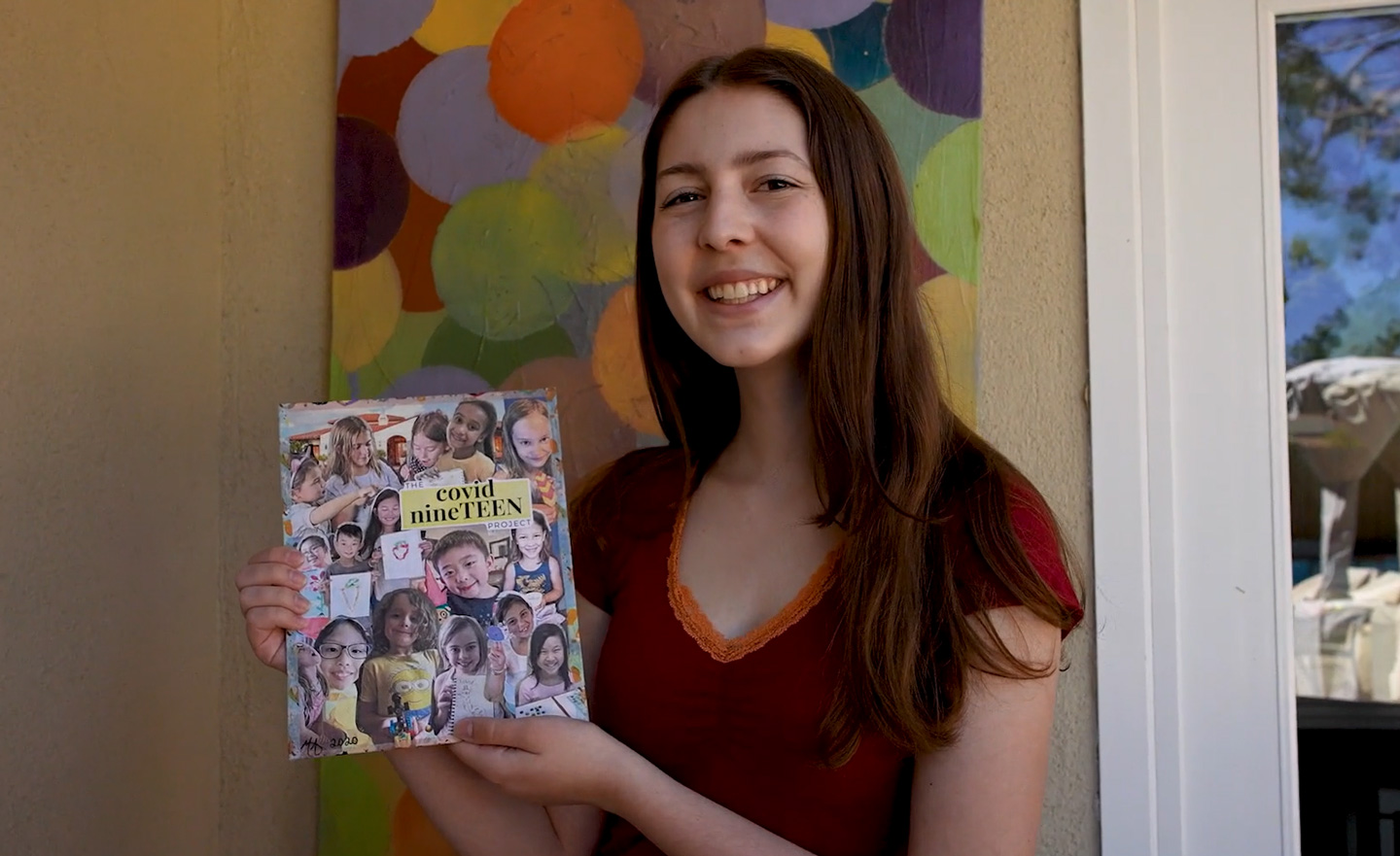 Sarah holding up a Covid nineTEEN collage of student photos.