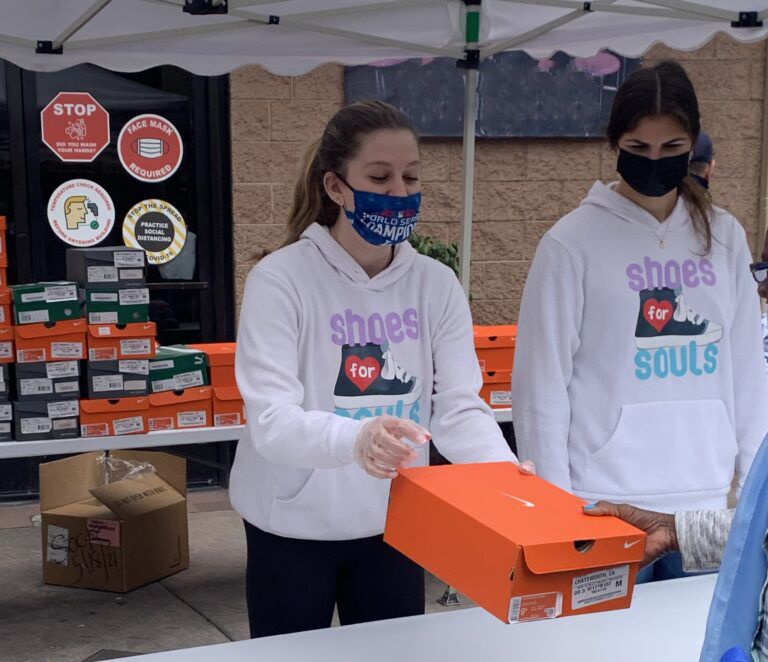 Two teen volunteers hand a box of shoes to someone.