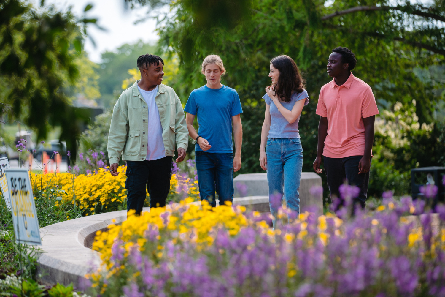 Danielle Wasserman walking outside in a flower garden with 3 high school students.