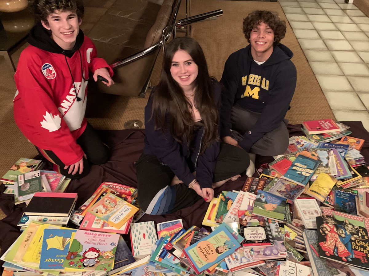 Alana and two other teen volunteers with a pile of donated books.