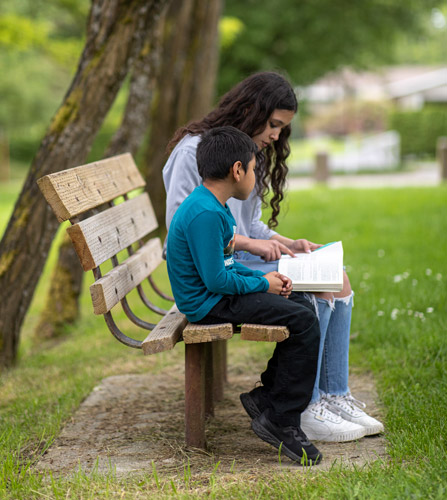 Sophies sits with a young student on a bench outside looking at homework.