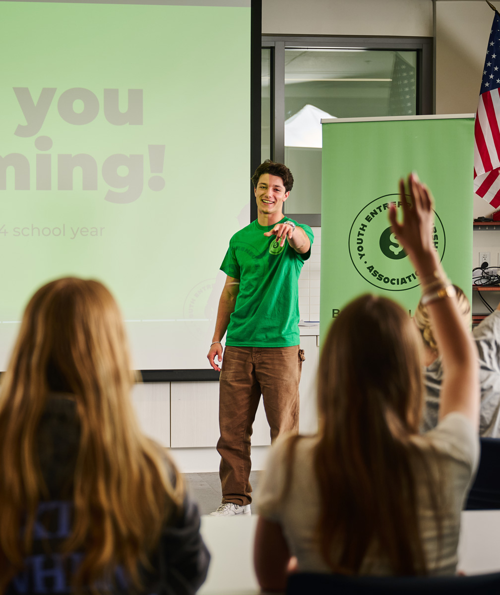 Mason Arditi stands in front of a classroom of students pointing at a girl with a raised hand.