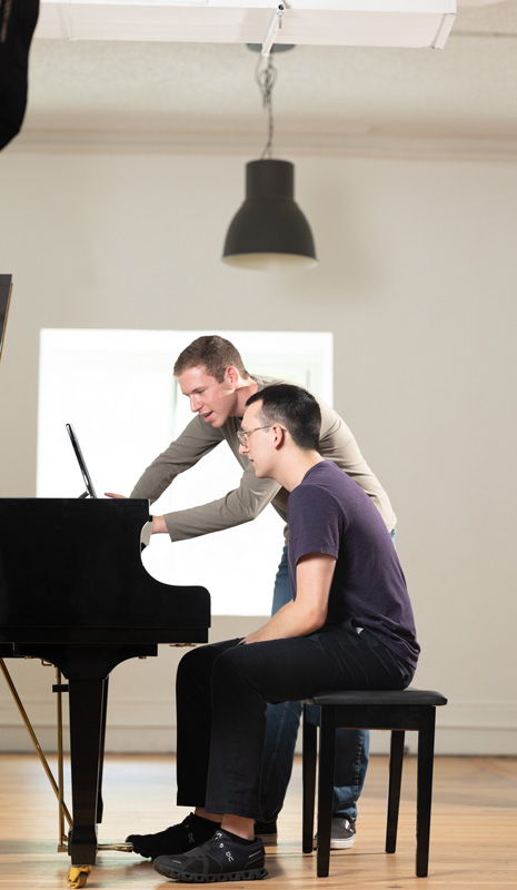 Jonah Cohen leans over a student at the piano.