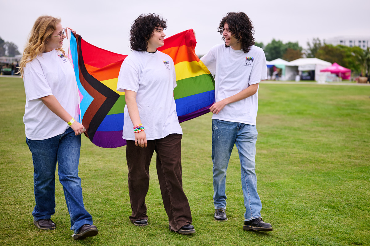 Zoey Schwartz walks with 2 friends who hold a progress pride flag behind her.