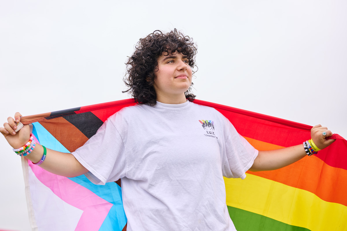 Zoey Schwartz poses with a progress pride flag behind her.