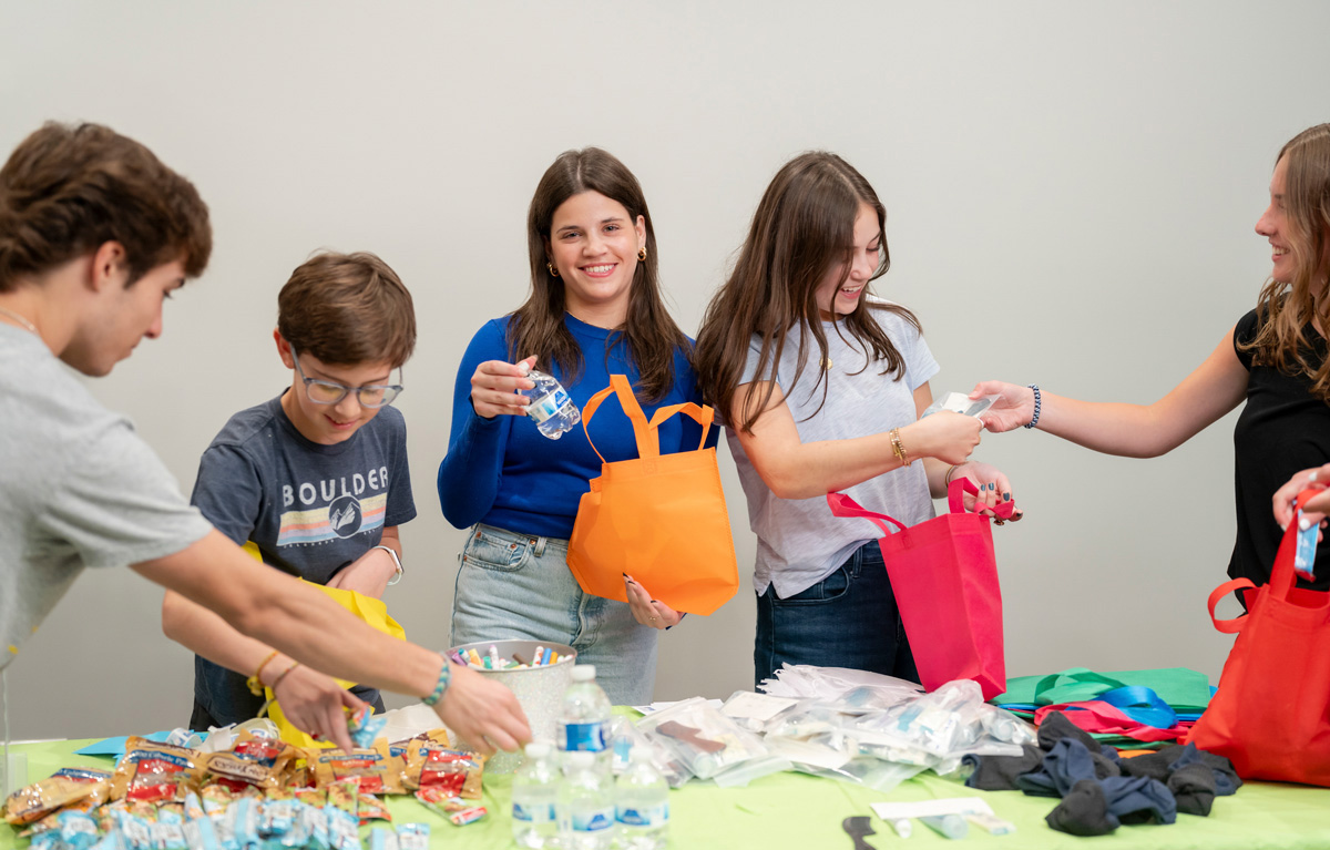 Group packing colorful bags at a table with snacks and supplies—suggests a community or volunteer event.