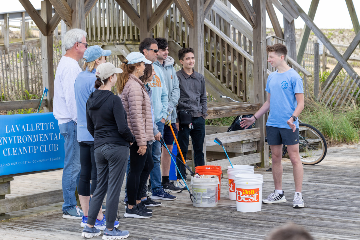 Group gathered by a wooden structure at the beach, participating in a Lavallette Environmental Cleanup Club event with buckets and trash pickers.