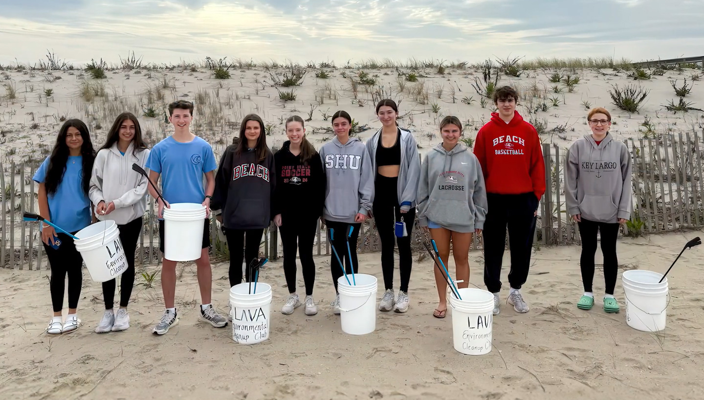 Landon stands with several teenagers on the beach, all with cleanup supplies.