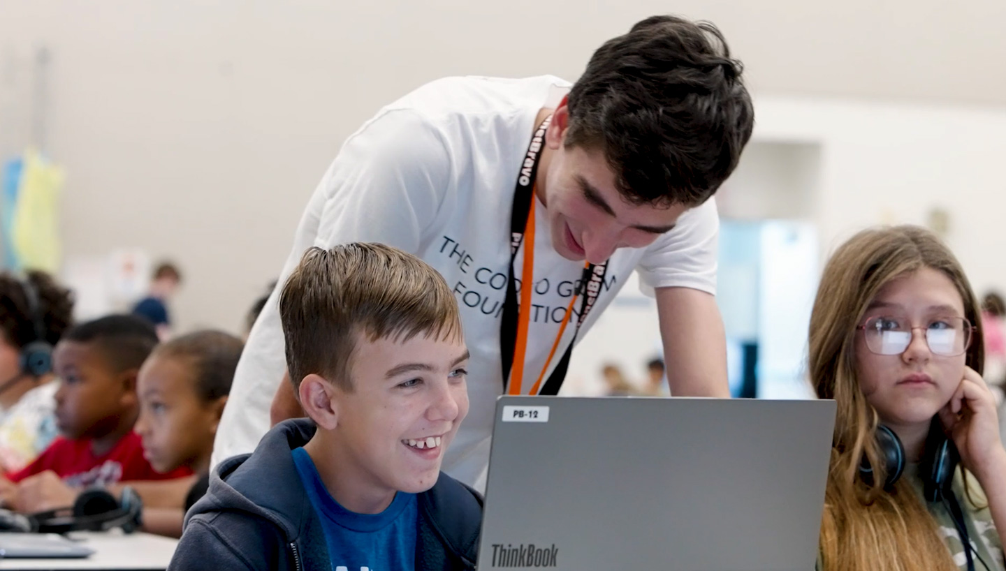 Jack leans over a student working on a laptop computer in a classroom