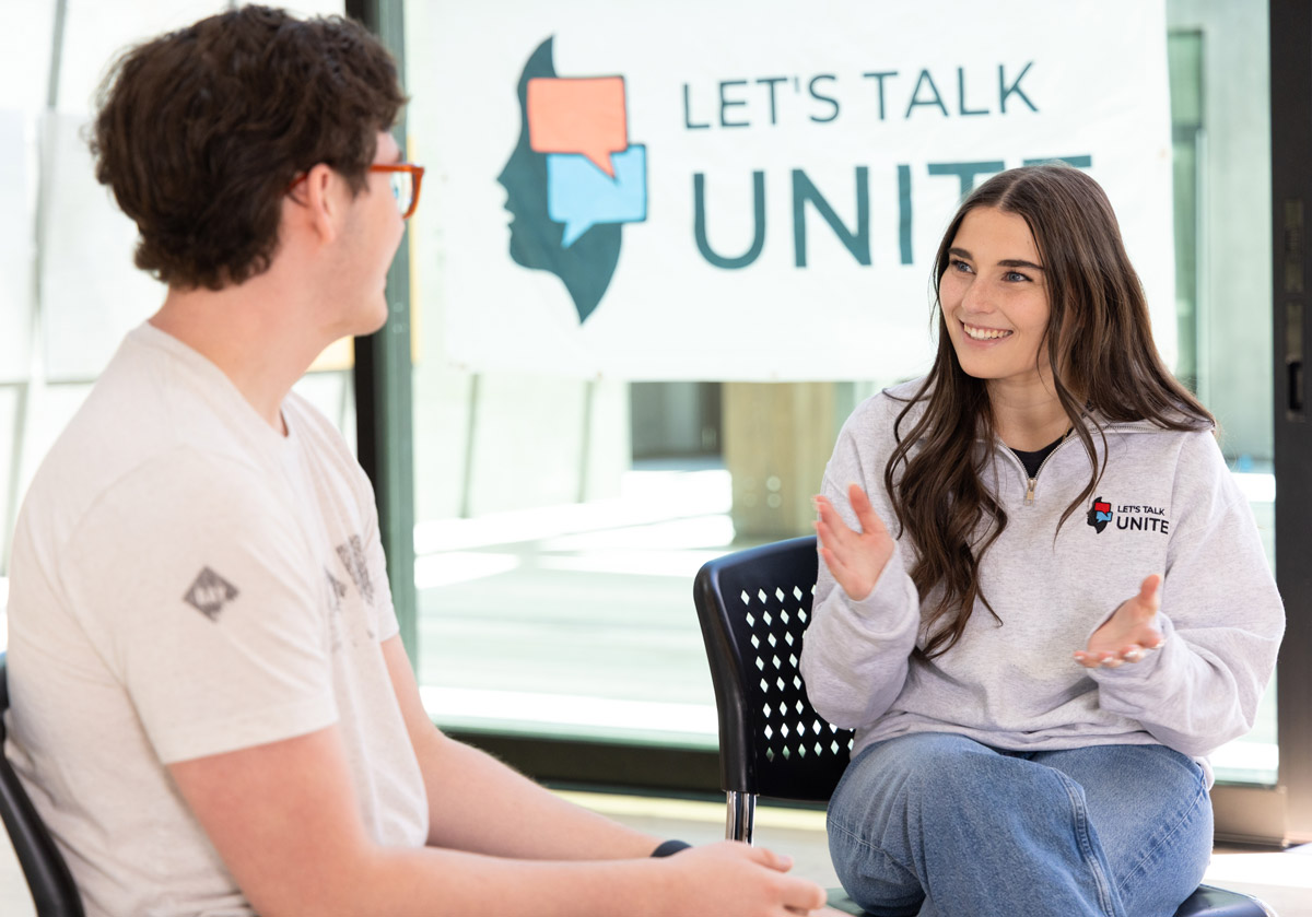 Teen talks with another student during a Let's Talk Unite conversation in a school setting.