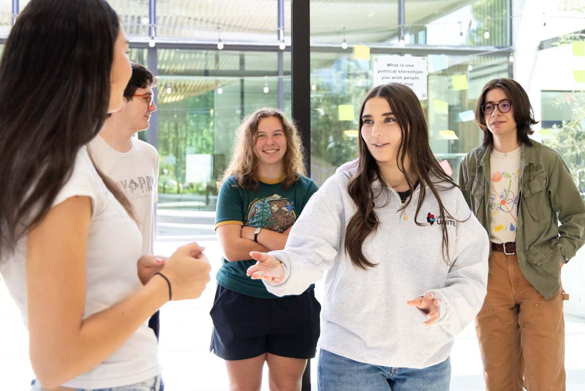 Teen leads a Let's Talk Unite discussion with a small group of students in a bright meeting space.