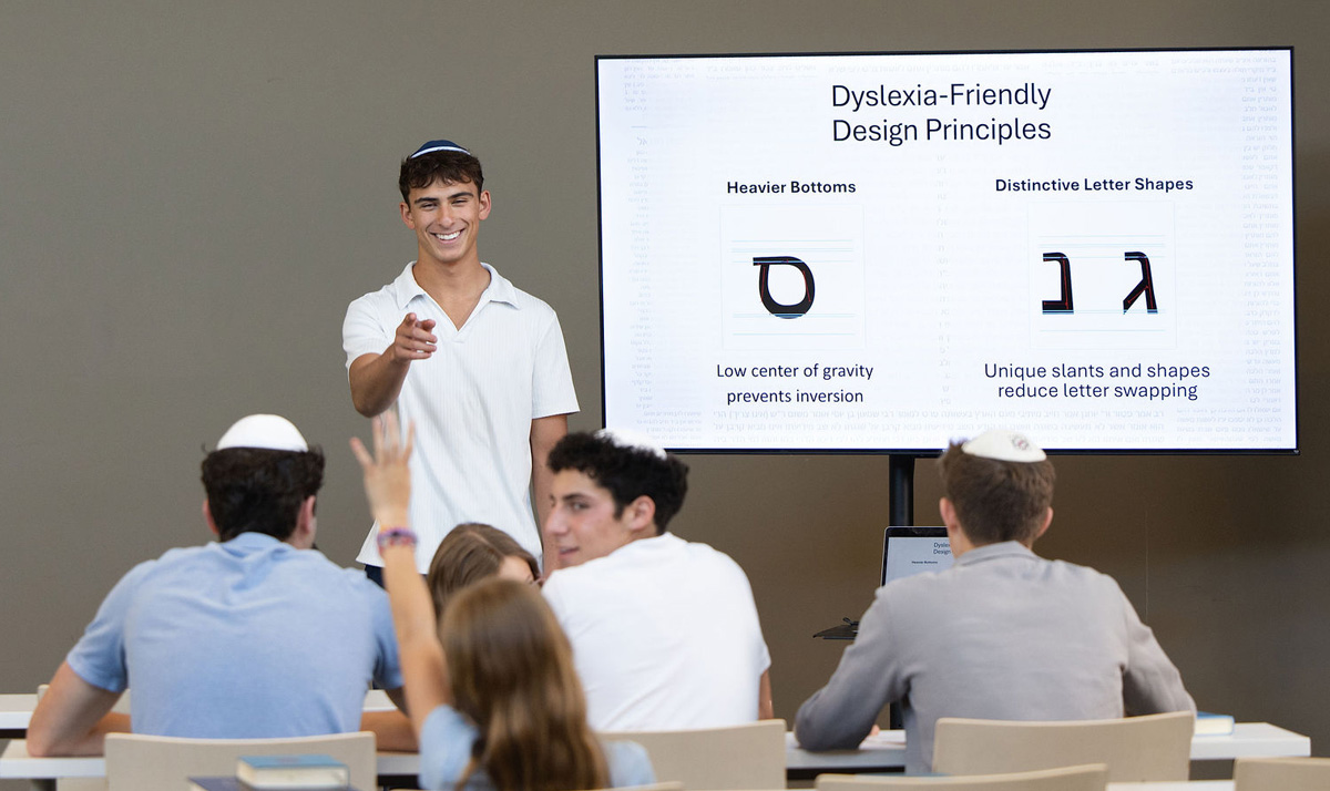 A presenter smiles and points toward students as a slide on dyslexia‑friendly design principles displays behind them.