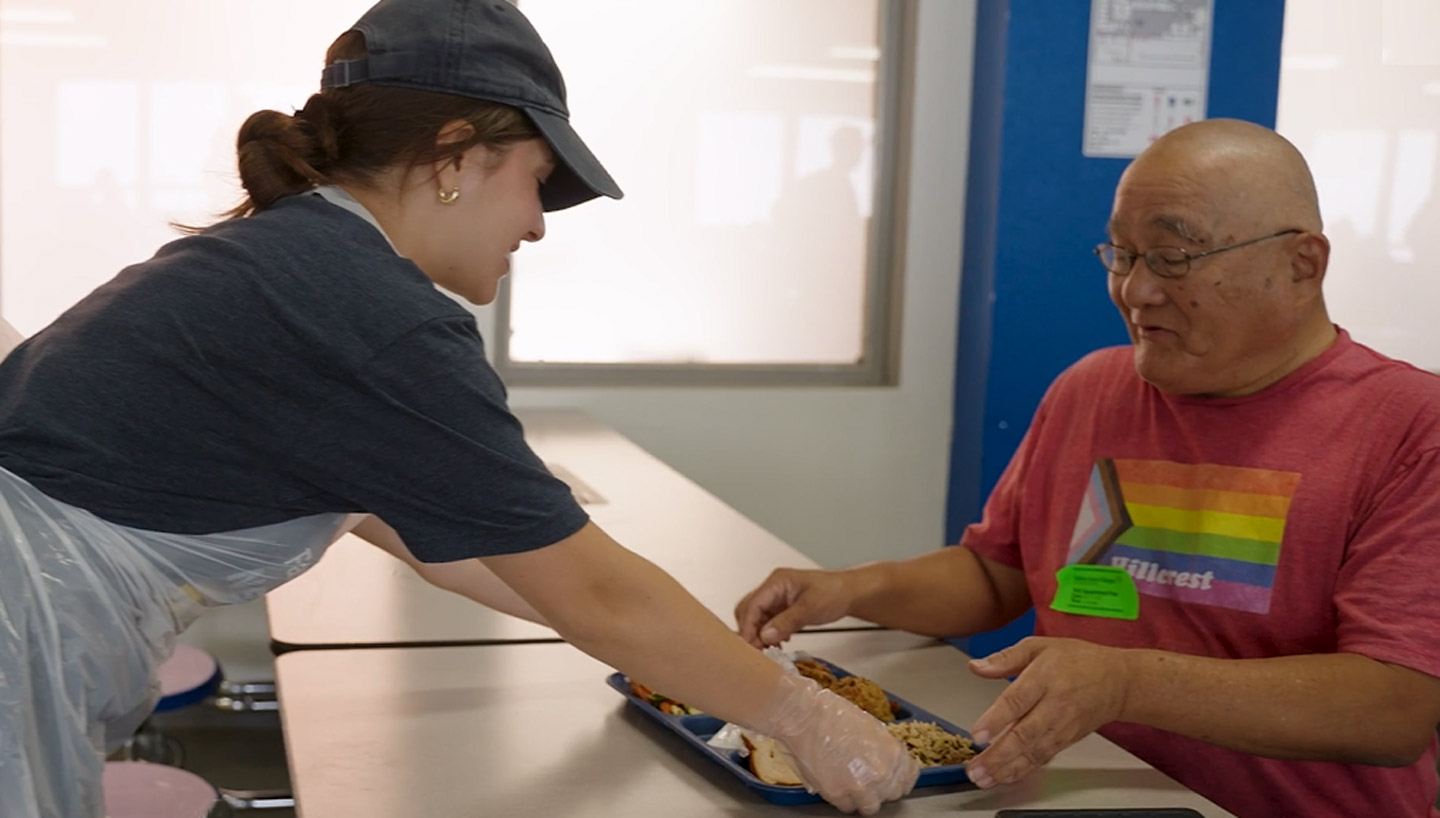 Person handing a lunch tray to another person in a cafeteria